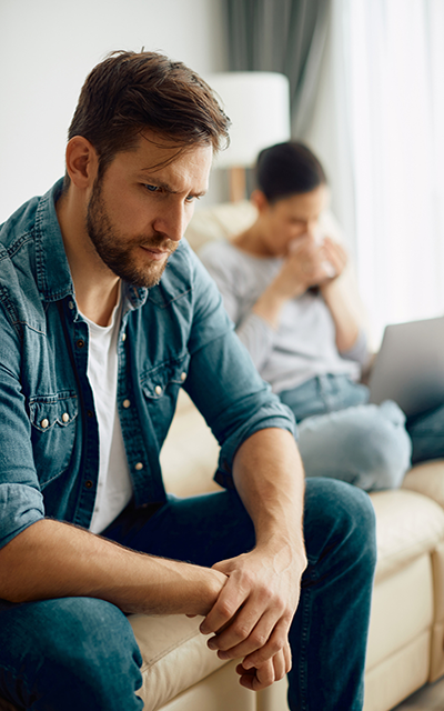 Distraught man sitting on the sofa and thinking while having relationship problems with his wife at home.