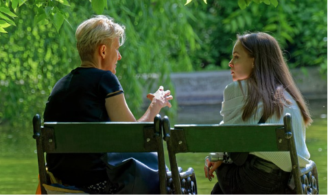 mother talking to teenage daughter on park bench